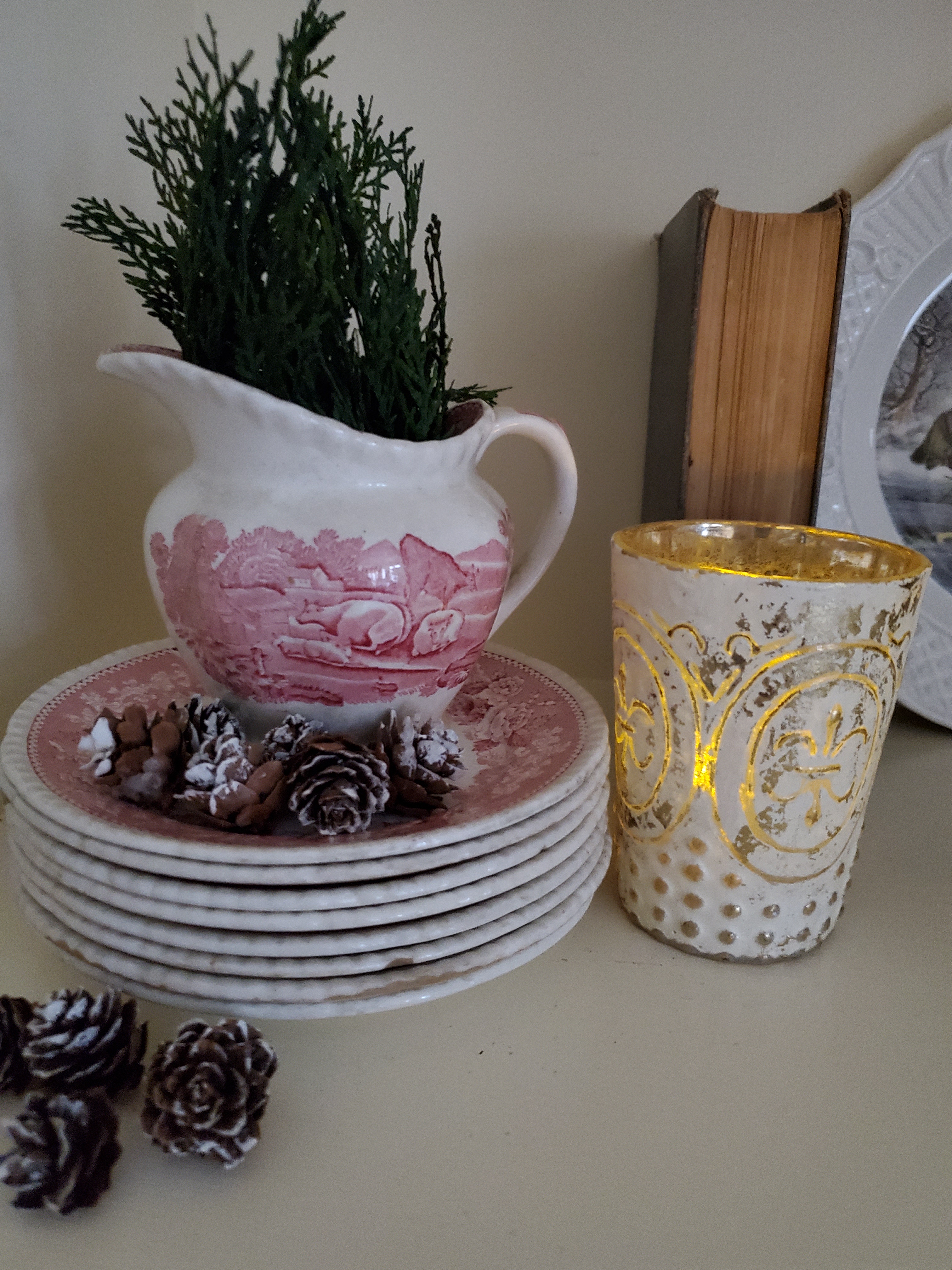 a small pitcher with greens small pincones and a votive witha candle for warm winter touches