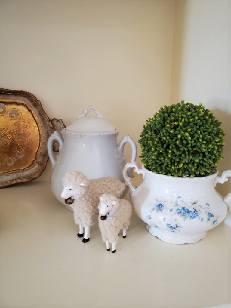 sheep near a thrifted blue and white sugar bowl with a green moss ball