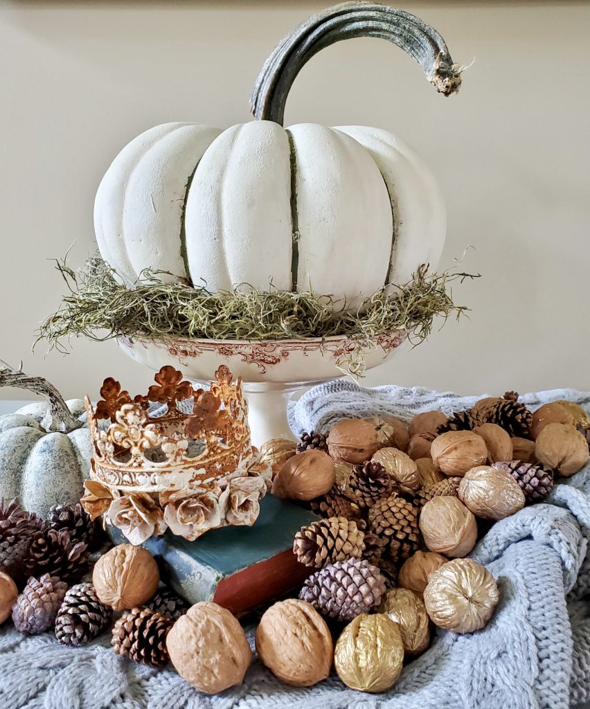 A pumpkin in a dish with walnuts and pinecones.  Crowns on books are perfect for a simple home addition