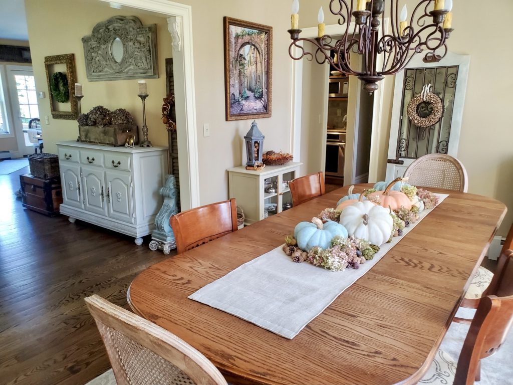 picture of natural fall decor of the dining room. the dining room table again the same way as above
showing the family room attached for an open floor plan
a door leaning on the dining room wall with an acorn wreath and a small cabinet