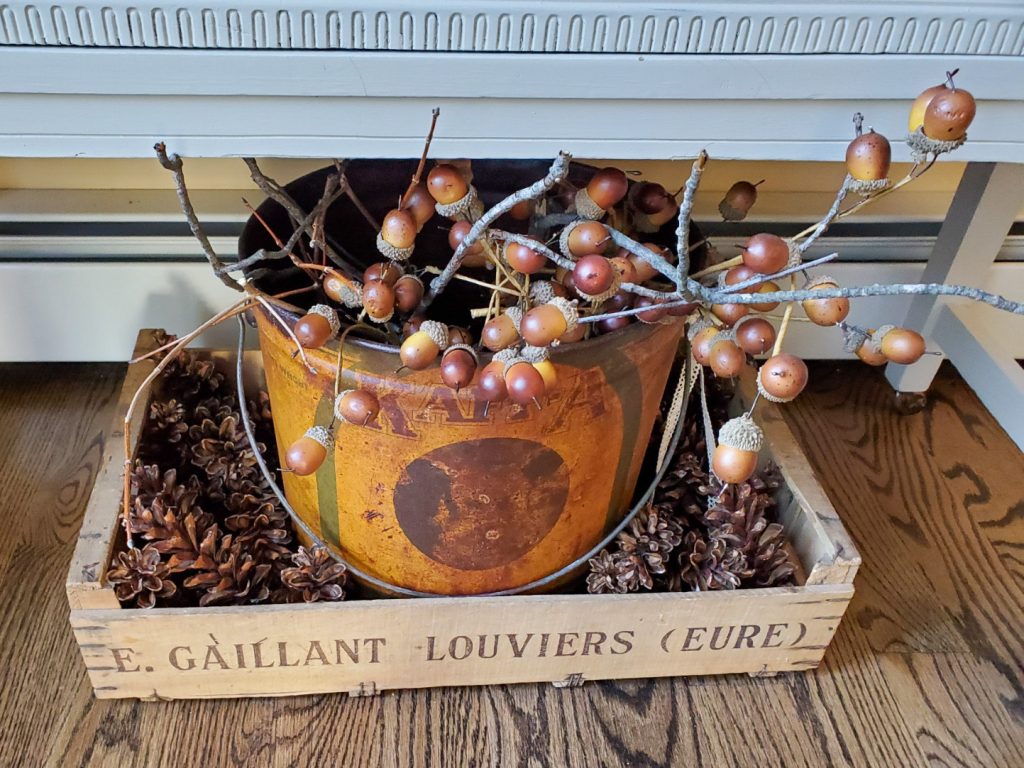 close up fall decor inluding a bucket filled with acorn branches bbear sticks for natural fall decor.
A crate filled with pine cones
