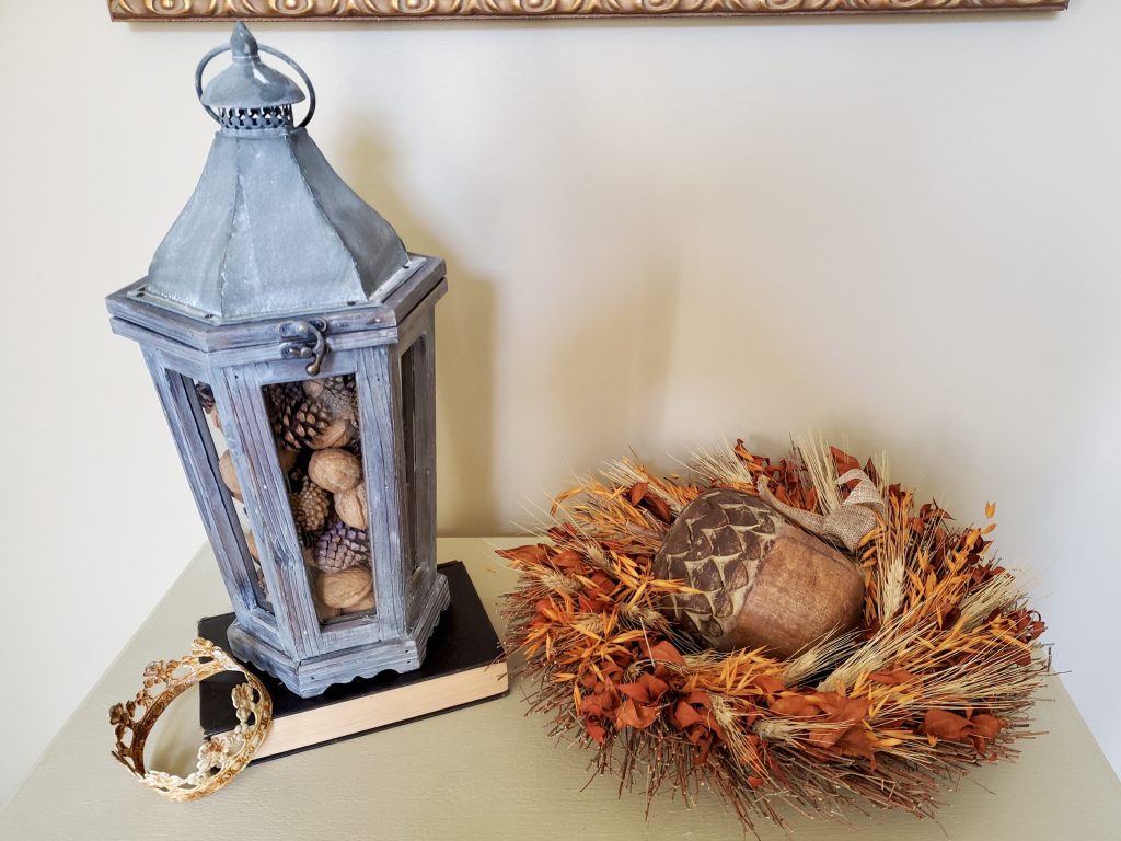 a close up of a lantern filled for natural fall decor
a large wooden acorn inside a wreath laying on the cabinet