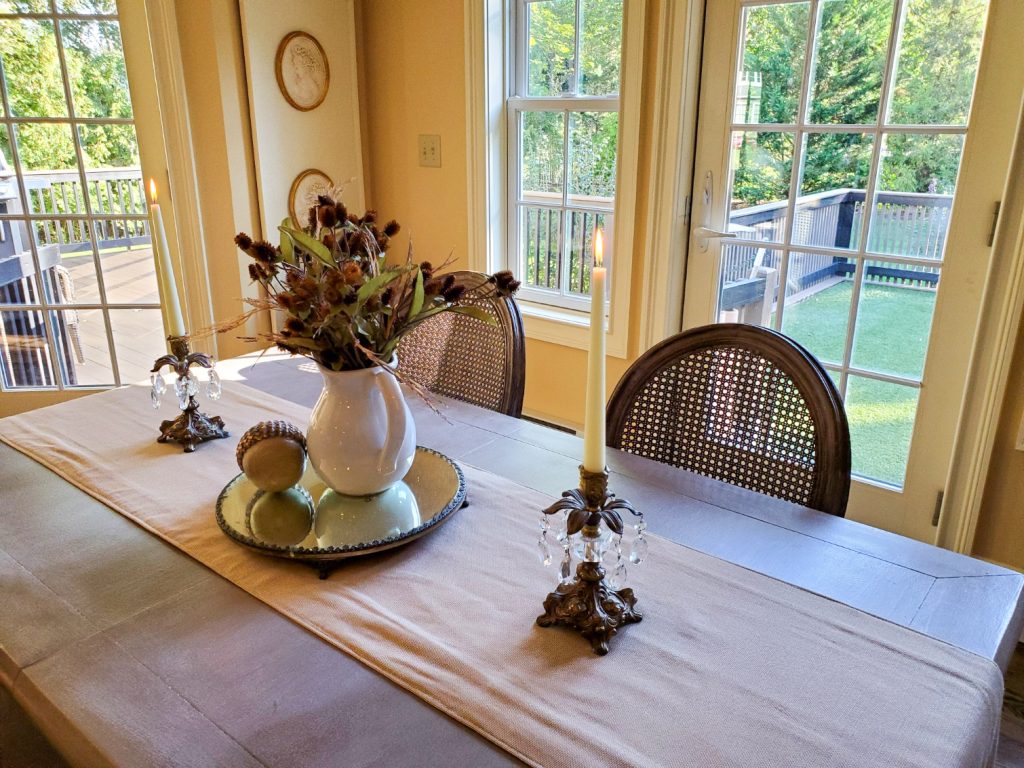 Table with candles lit with a centerpiece of a pitcher, a mirror and an acorn for fall decor
Candles are lit on the table