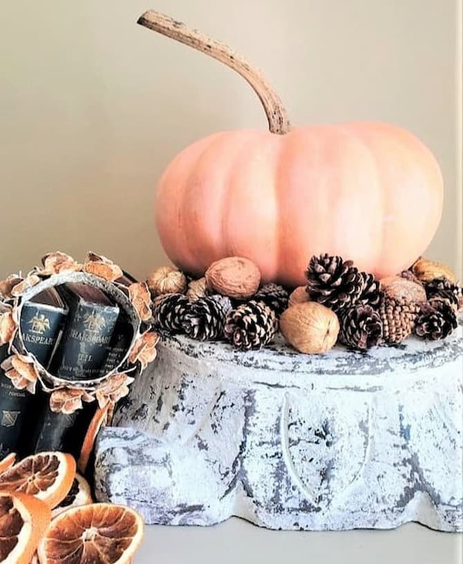 chalk-paint-on-pumpkins-is-a-sustainable-choice-pumpkin-on-pedestal-with-nuts-oranges-pinecones