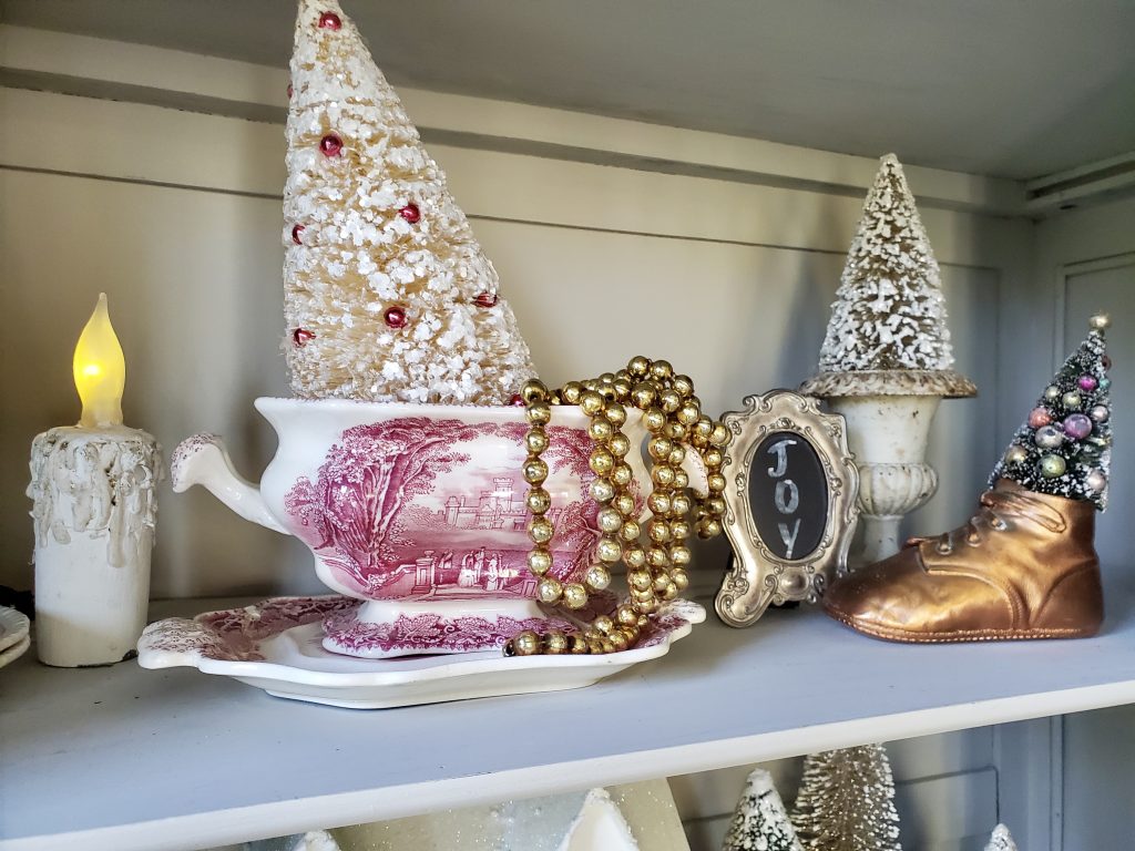 a flameless candle, transferware and a small frame that says JOY on it inside the vintage French Christmas hutch