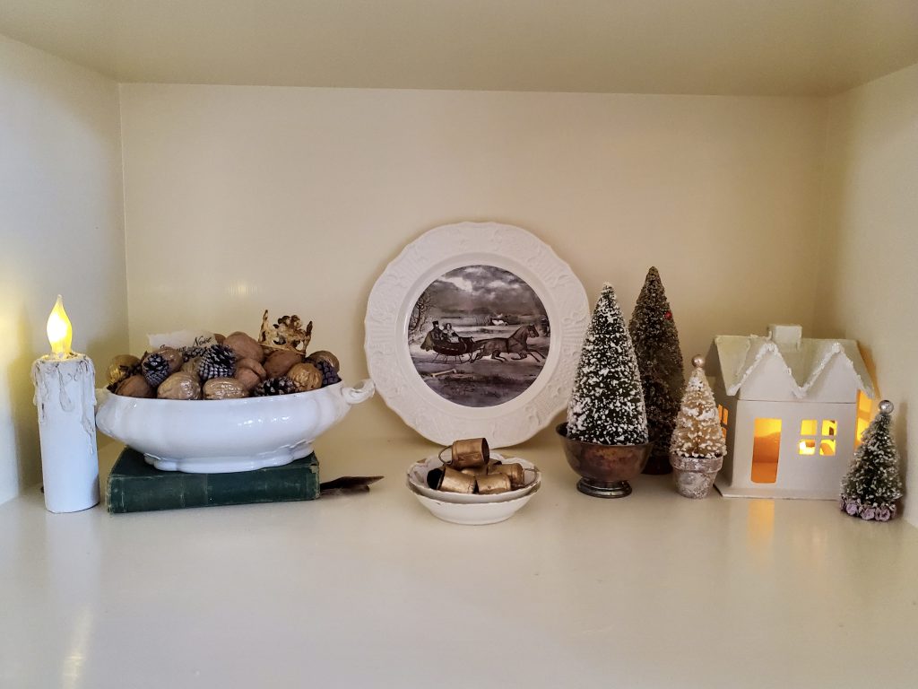 a flameless candle,tureen filled with pinecones. A white dish with a winter scene. small sidhes with bells inside and bottle brush trees for a vintage French CVhristmas