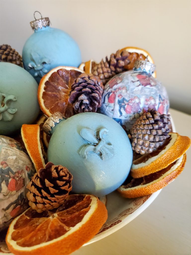 the finished ornaments dispaly in a bowl with orange slices and pinecones