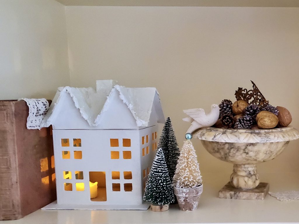 showing a white house with bottle brush trees. An Alabaster bird bath filled weith pinecones and walnuts