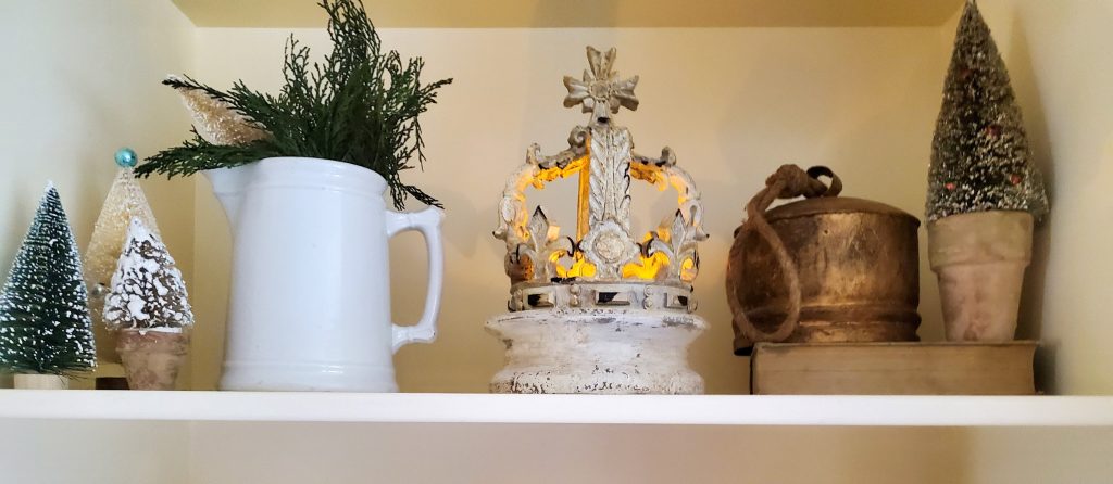 shelf with bottle brush trees, a pitcher, crown with a candle. A vintage bell and book for a vintage French Christmas