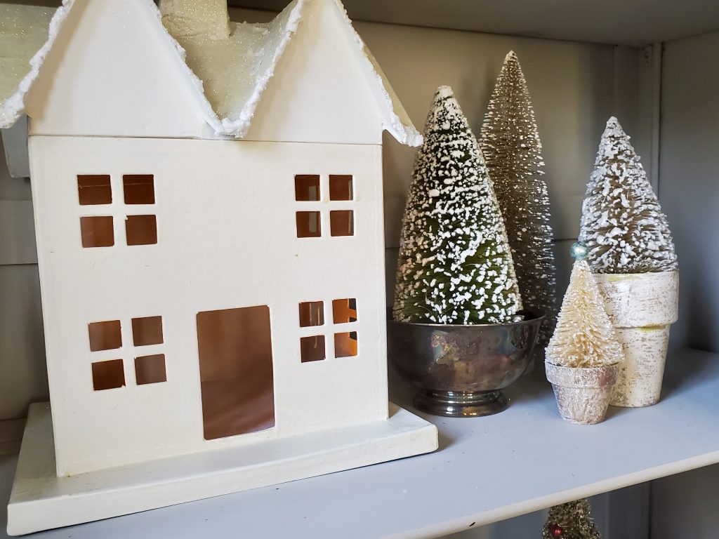 a white house with bottle brush trees in a silver bowl nd flower pots in a vintag Christmas