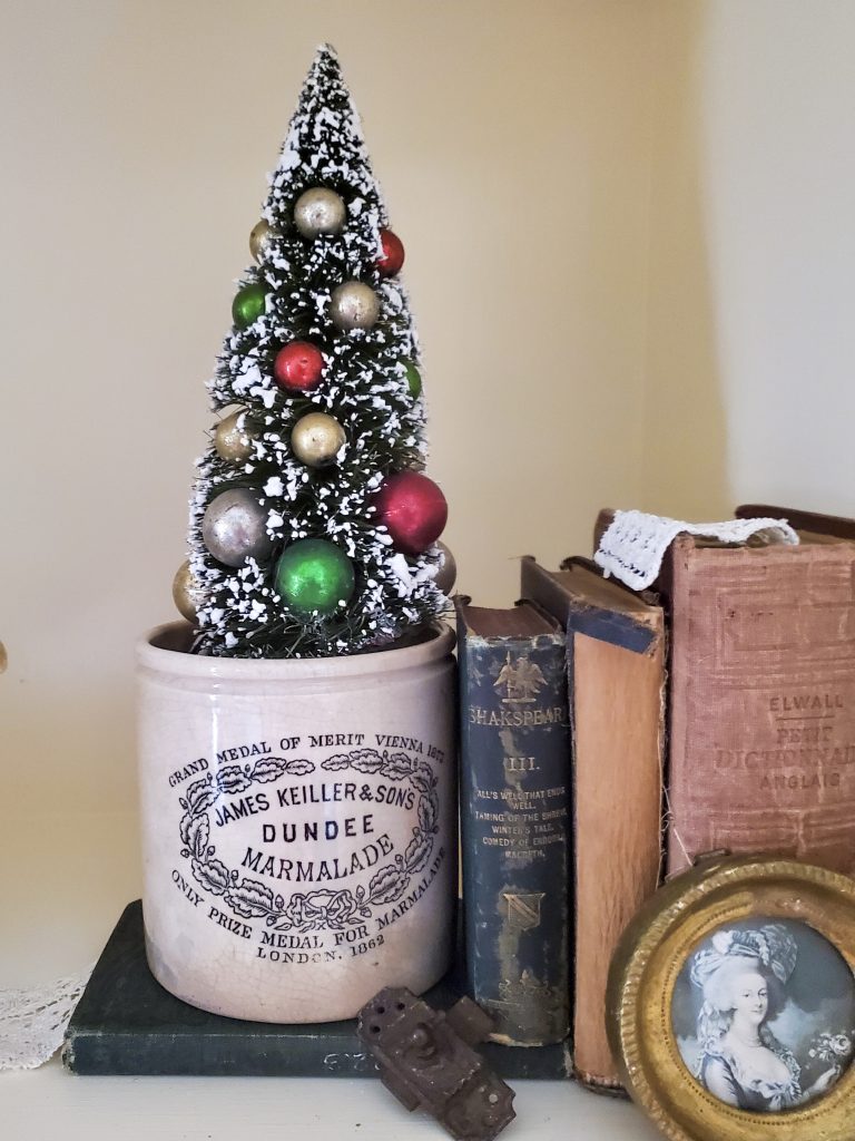 close up of a bottle brush tree in a crock. Books and a small lock