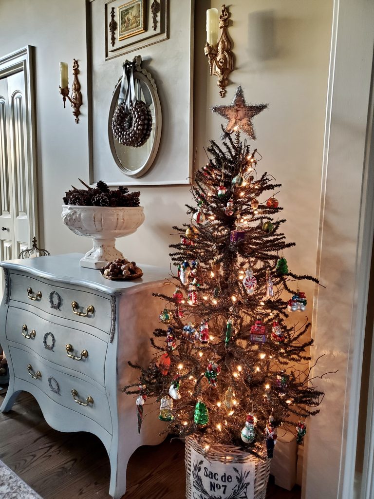 a cristmas tree in basket next to the bombay chest