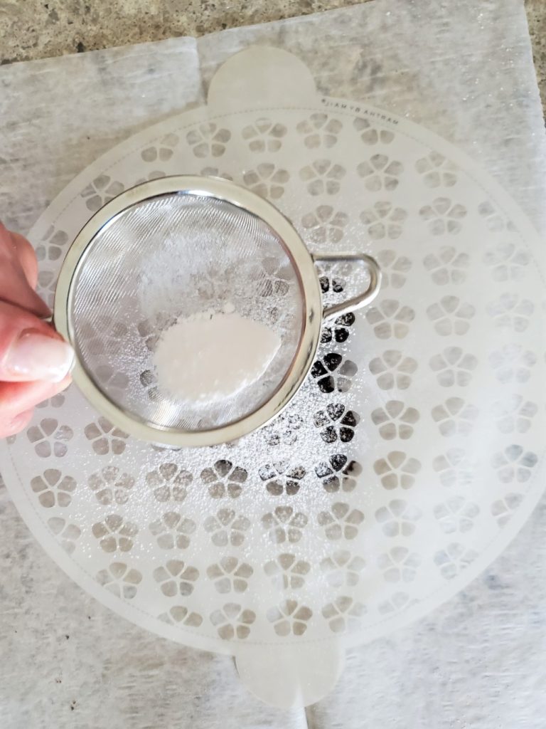Sprinkling the brownies with confectioner sugar with a small mesh strainer over a floral cake stencil