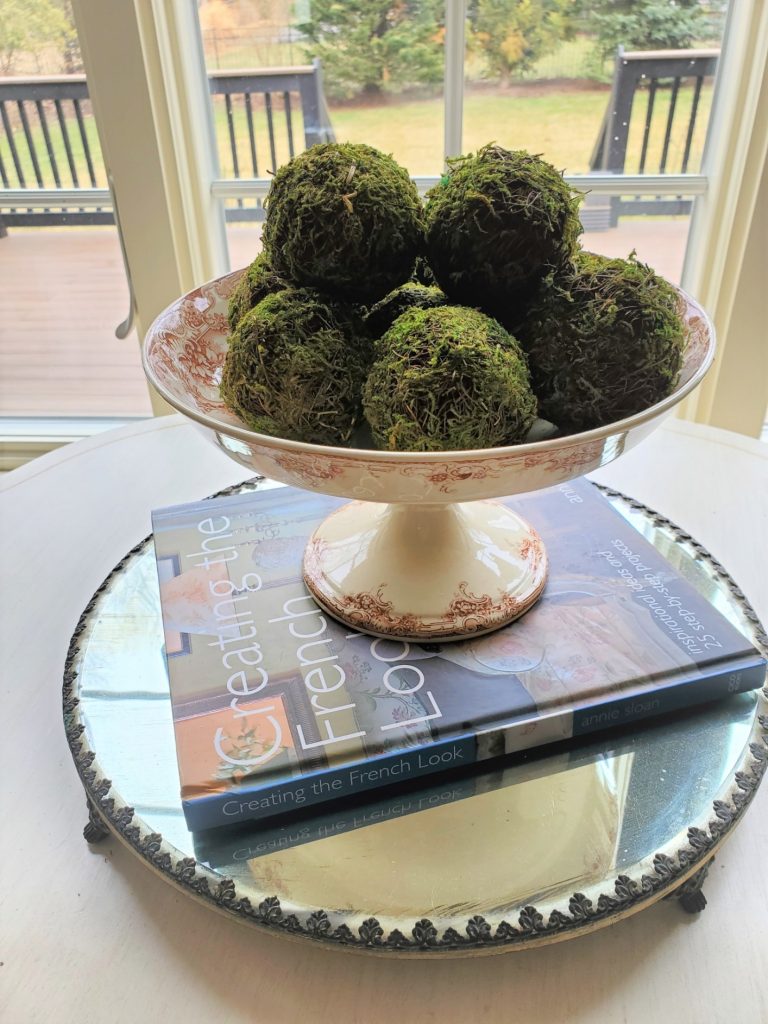 Moss balls in an antique compote dish on a plateau mirror for spring