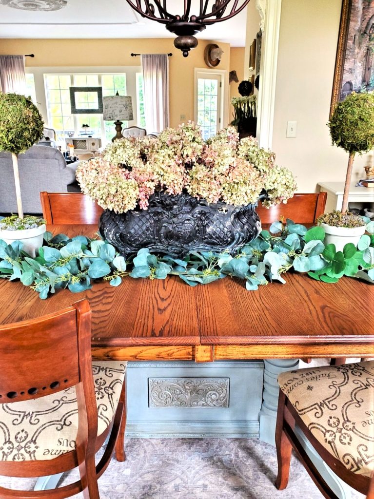 as-a-centerpiece-with-hydrangeas-in-cast-iron-pot-and-the-two-topiaries-with-garland