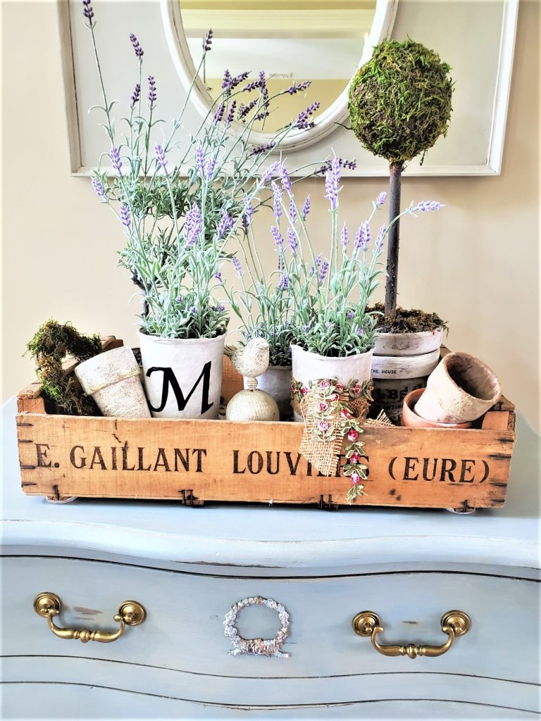 a closer look at the antique flower crate filled with lavender pots, terracotta pots, a topiary, small wreath and a bird finial