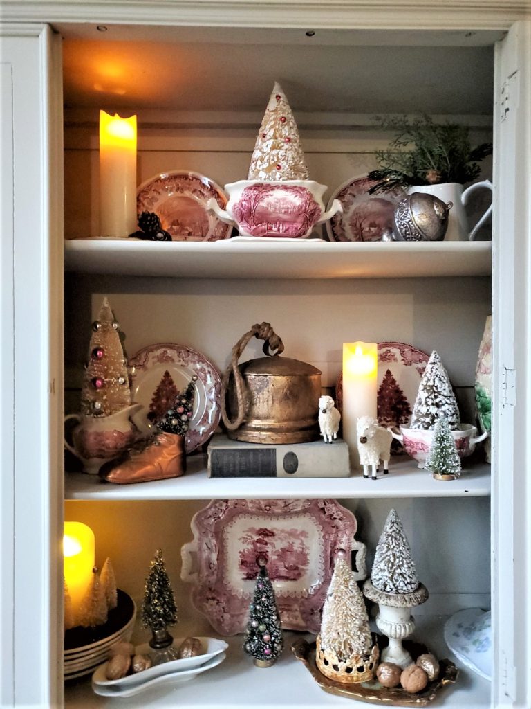 the candles lit inside the Christmas hutch with bottle brush trees, walnuts, antique dishes
