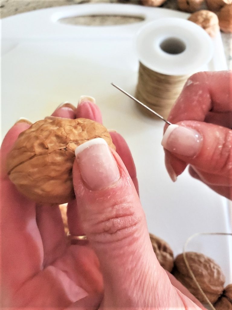 Showing the thread, neeedle and the needle going through the walnut for the easy fall garland