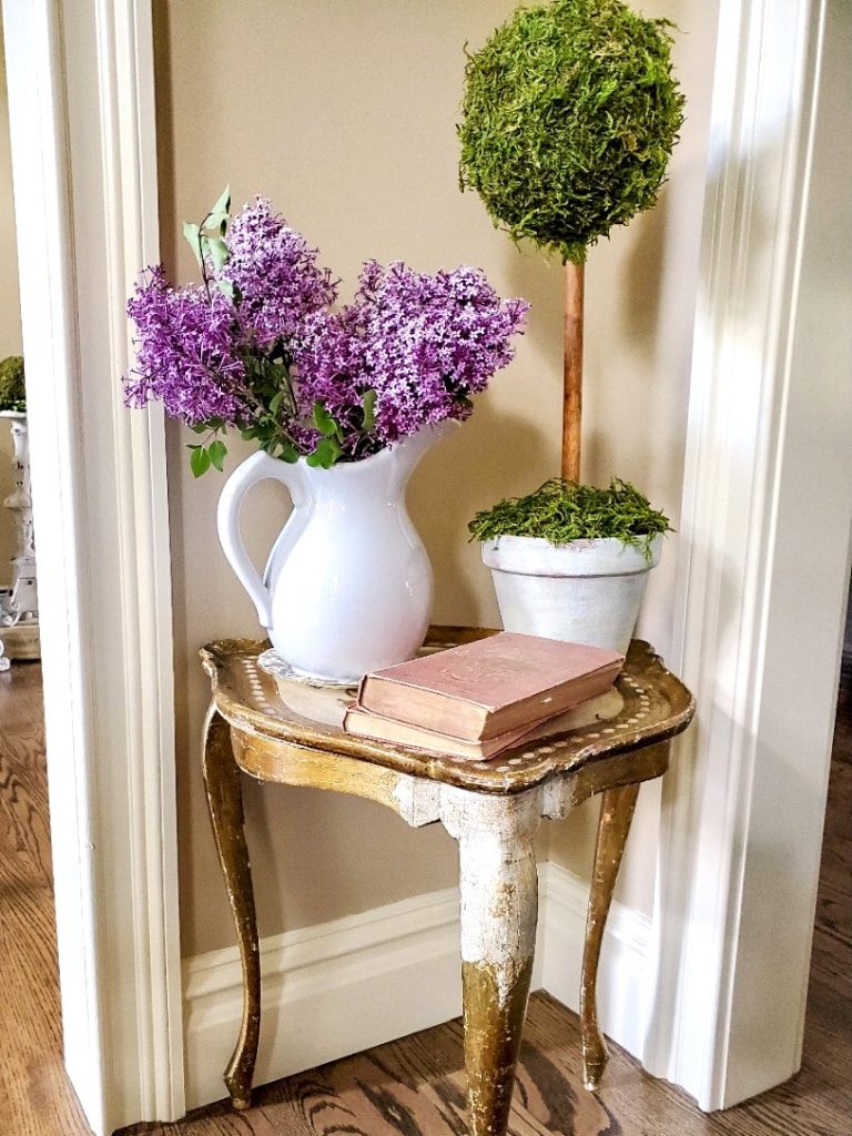 pitcher-filled-with-lilacs-on-a-florentine-table-with-a-topiary