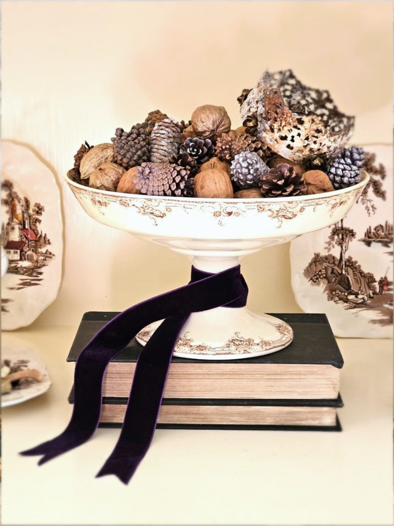 compote-filled-with-pinecones-walnuts-and-a-crown-on-books-dark-plum-velvet-ribbon