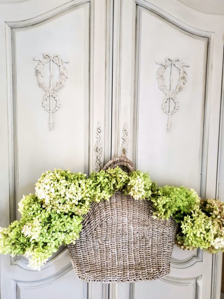 dried-green-hydrangeas-in-a-basket-hanging-from-handles-on-armoire