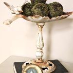 don't-miss-out-on-easy-spring-decorating-ideas-closer-look-at-moss-balls-in-cast-iron-bird-feeder-sitting-on-a-book-with-a-small-picture-featured-image